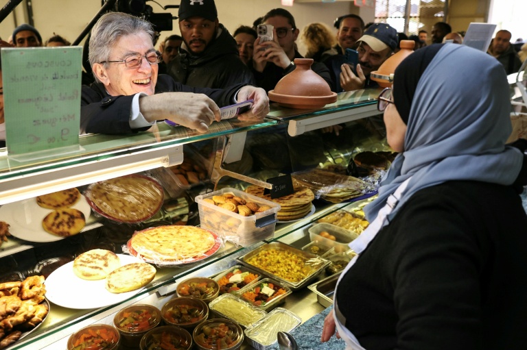Jean-Luc Mélenchon (g), leader de La France Insoumise (LFI), parle avec une vendeuse lors d'une visite au marché de Choisy-le-Roi, le 2 novembre 2025 dans le Val-de-Marne
