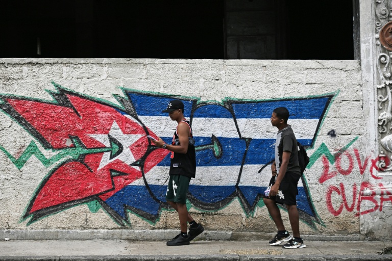 Deux jeunes passent devant un mur arborant un drapeau cubain, le 14 juillet 2026 à La Havane, lors d'une panne d'électricité nationale à Cuba