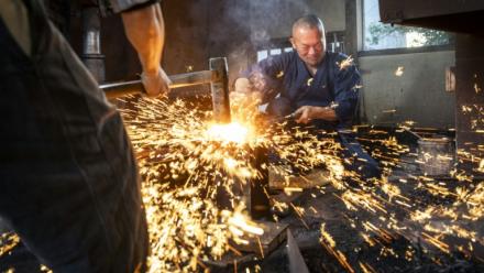 Le forgeron Akihira Kawasaki (d) maintient l'acier sur une enclume tandis que son apprenti Toru Watanabe martèle le métal pour forger des lames de katana, le 9 janvier 2026 à Misato, au Japon