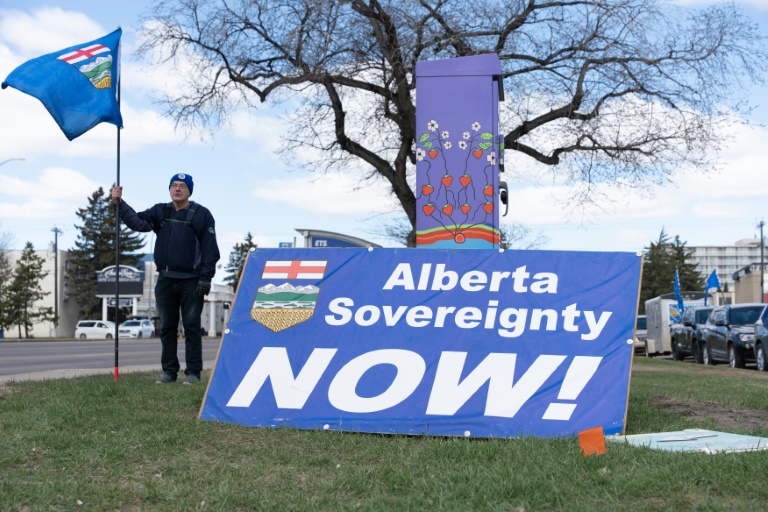 Un partisan séparatiste tenant un drapeau, à côté d'une pancarte réclamant la souveraineté de la province de l'Alberta 