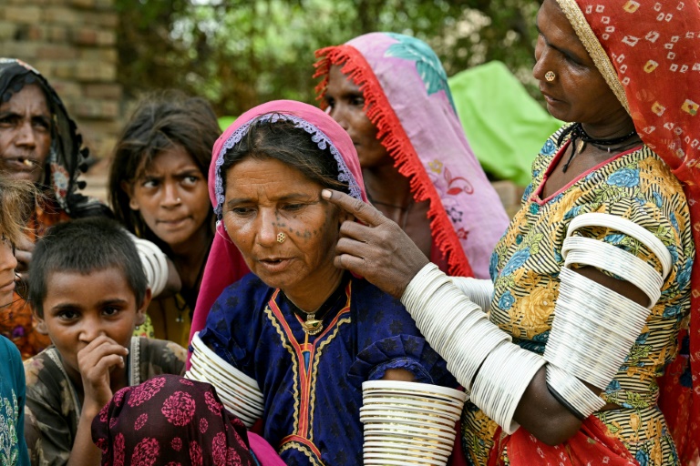 Une villageois en tenue traditionnelle montre un tatouage indigène encré sur le visage de Reshma (c) dans le village de Ponjo Kolhi, près d'Umerkot, un district à majorité hindoue, le 14 juillet 2025 au Pakistan