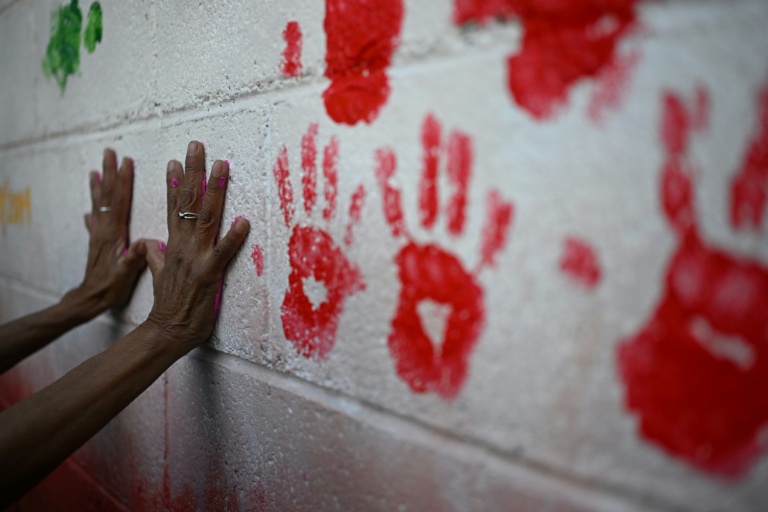 La mère d'une personne disparue pose ses mains couvertes de peinture lors de l'inauguration d'une fresque en hommage aux personnes disparues, à l'Université du Salvador, à San Salvador, le 19 mars 2026