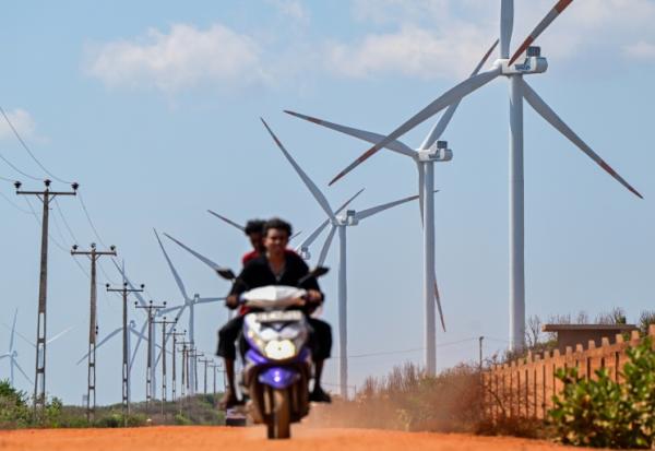 Cette photo, prise le 2 octobre 2026, montre un motard passant devant des éoliennes installées le long d'une route de la péninsule de Mannar, au Sri Lanka