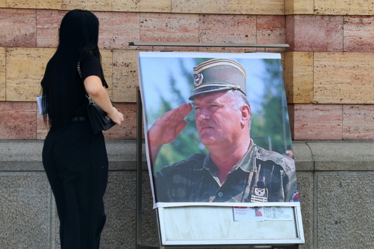 Une femme regarde un portrait de l'ancien chef militaire des Serbes de Bosnie, Ratko Mladić, devant la cathédrale orthodoxe de Banja Luka, en Bosnie, le 28 août 2026, au lendemain de sa mort à l'âge de 84 ans dans un hôpital pénitentiaire de La Haye