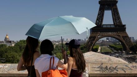 Des touristes se protègent du soleil sous un paraplluie devant la Tour Eiffel lors d'une vague de chaleur à Paris, le 27 mai 2026