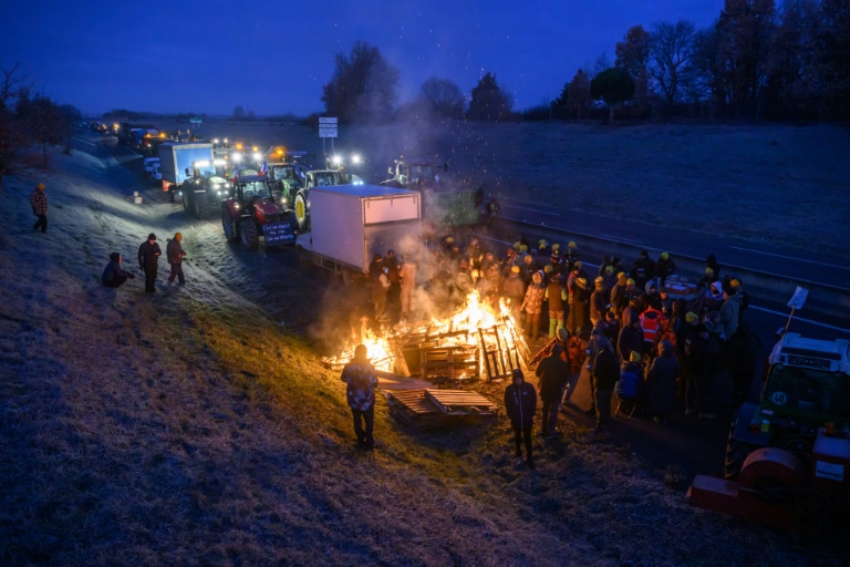 Des agriculteurs se réchauffent autour d'un feu alors qu'ils sont empêchés par les gendarmes d'entrer dans Toulouse, près de Leguevin, le 7 janvier 2026 