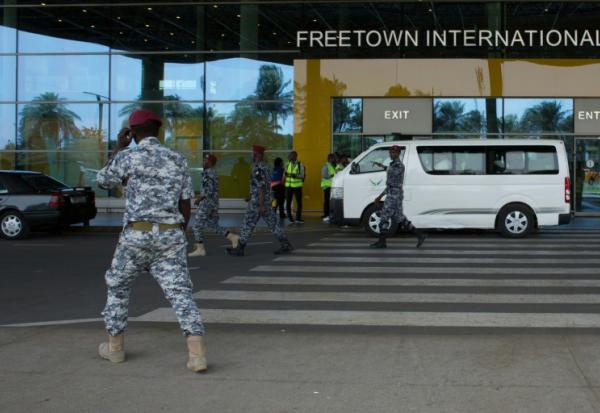 Des agents de sécurité escortent des migrants vers un centre de l'Agence nationale de santé publique (NPHA) après leur arrivée à l'aéroport international de Freetown, le 20 mai 2026 à Lungi, en Sierra Leone