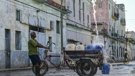 Un homme remplit des récipients d'eau à un point de ravitaillement public dans une rue de La Havane, le 5 octobre 2026
