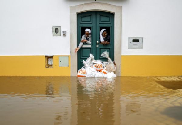Deux religieuses observent la rue depuis une porte renforcée par des sacs de sable pendant les indondations liées à la tempête Leonardo à Alcacer do Sal, au sud du Portugal, le 4 février 2026