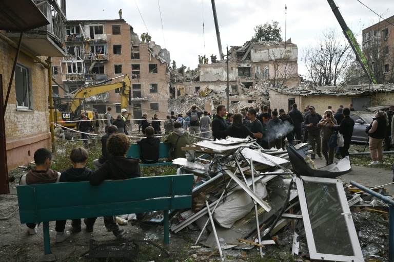 Des habitants observent des secouristes travailler dans les décombres d'un immeuble détruit par une frappe russe à Pryluky, en Ukraine, le 7 octobre 2026