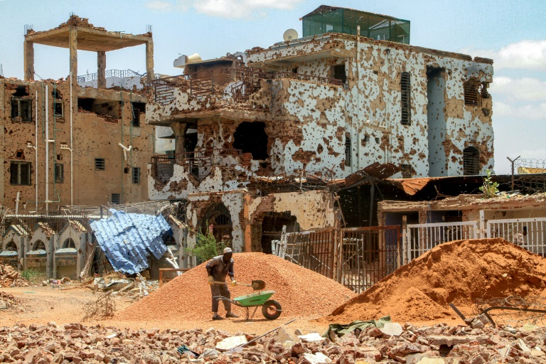 Un ouvrier pellette des cailloux dans une brouette près d'un bâtiment fortement endommagé de la banlieue de Lambab, à la périphérie de Khartoum, le 30 juillet 2025 au Soudan