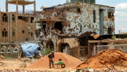 Un ouvrier pellette des cailloux dans une brouette près d'un bâtiment fortement endommagé de la banlieue de Lambab, à la périphérie de Khartoum, le 30 juillet 2025 au Soudan