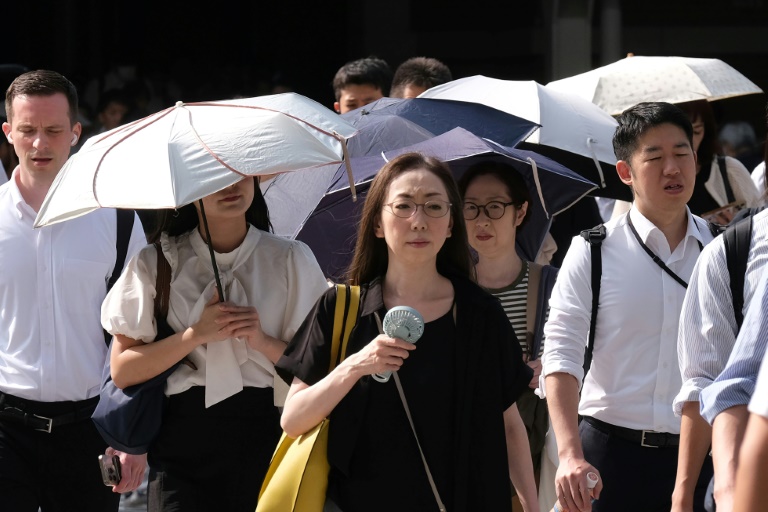 Une femme, un ventilateur miniature à la main, se rend au travail par une matinée chaude et ensoleillée à Tokyo, le 6 août 2025 au Japon