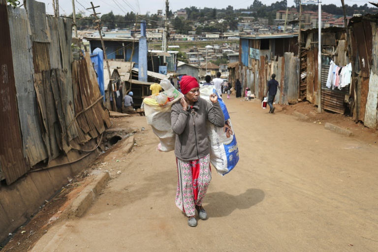Magret John porte un sac de déchets plastiques usagés vers un point de collecte de l'ONG Human Needs Project (HNP) dans le bidonville de Kibera, à Nairobi, le 11 août 2025 au Kenya