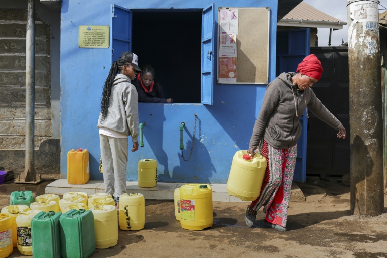 Margaret John (d) récupère des jerrycans d'eau propre à un point de distribution après avoir échangé des points gagnés en livrant des déchets plastiques à un point de collecte de l'ONG Human Needs Project (HNP) dans le bidonville de Kibera, à Nairobi, le 11 août 2025 au Kenya