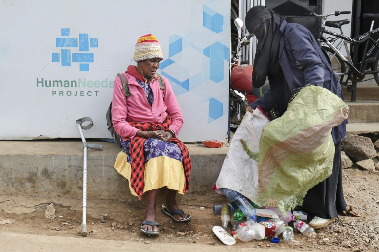 Molly Aluoch (c) remet un sac de déchets plastiques usagés à un responsable de l'ONG Human Needs Project (HNP) dans le bidonville de Kibera, à Nairobi, le 11 août 2025 au Kenya
