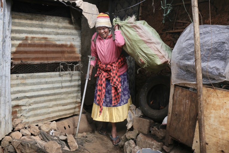 Molly Aluoch s'appuie sur une béquille pour porter un sac de déchets plastiques usagés collectés dans le bidonville de Kibera, à Nairobi, le 11 août 2025 au Kenya