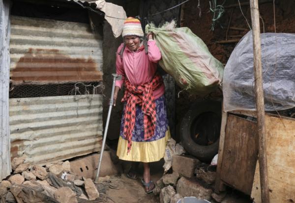 Molly Aluoch s'appuie sur une béquille pour porter un sac de déchets plastiques usagés collectés dans le bidonville de Kibera, à Nairobi, le 11 août 2025 au Kenya