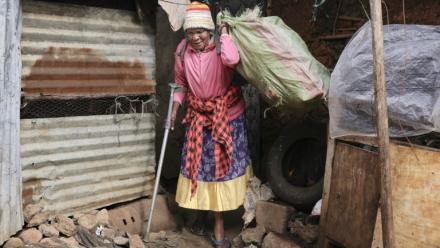 Molly Aluoch s'appuie sur une béquille pour porter un sac de déchets plastiques usagés collectés dans le bidonville de Kibera, à Nairobi, le 11 août 2025 au Kenya