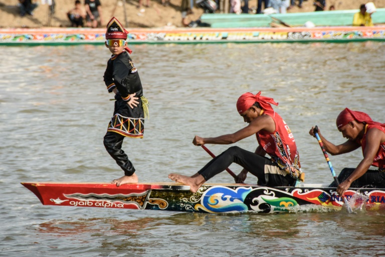 Rayyan Arkan Dikha danse à l'avant d'un bateau lors d'une course nautique traditionnelle, le 22 août 2025 sur la rivière Kuantan, dans la province indonésienne de Riau, sur l'île de Sumatra 