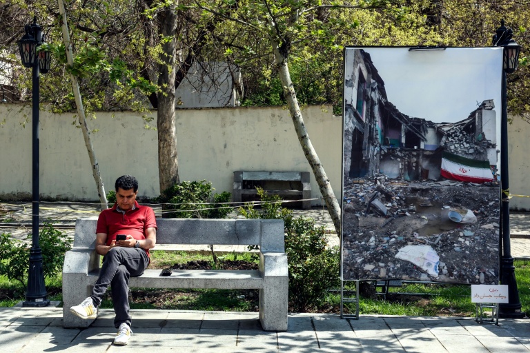 Un Iranien consulte son téléphone, assis sur un banc à côté d'une photo montrant 