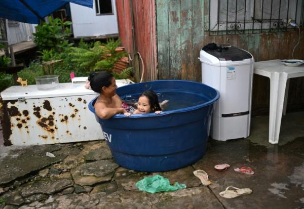 Une femme et sa fille se rafraîchissent dans une grande bassine remplie d'eau à Vila da Barca, un quartier pauvre bâti sur pilotis sur les rives du fleuve Guama à Belem, dans l'État du Para, le 5 novembre 2025 au Brésil