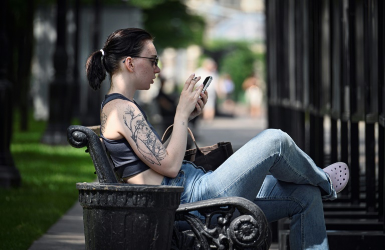 Une femme assise sur un banc utilise son smartphone à Moscou, le 30 juillet 2025