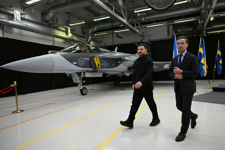 Le Premier ministre suédois Ulf Kristersson (d) et le président ukrainien Volodymyr Zelensky passent devant un avion de chasse Gripen à l'issue d'une conférence de presse conjointe à Linköping, en Suède, le 22 octobre 2025
