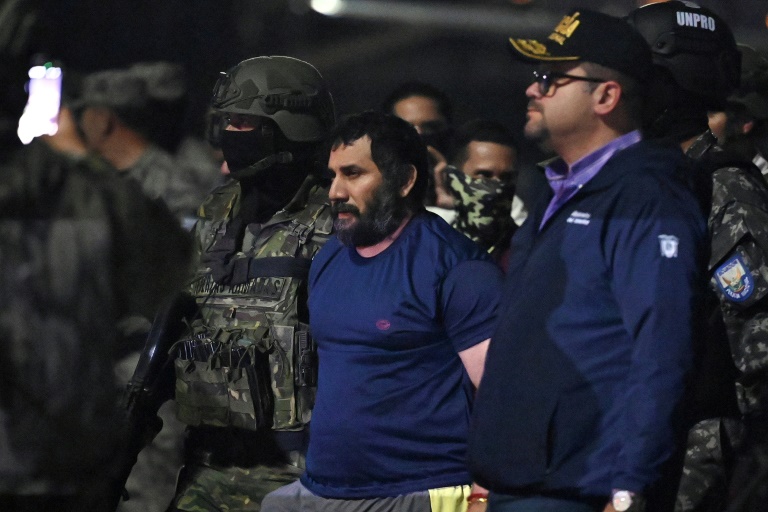 Le trafiquant de drogue Adolfo Macias (c), alias Fito, gardé par le ministre de l'Intérieur équatorien John Reimberg (2e d) et du personnel militaire à son arrivée à la base aérienne de Guayaquil, après sa recapture, le 25 juin 2025 à Manta, dans la province de Manabi, en Équateur 