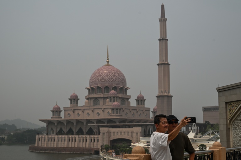 Deux personnes se prennent en photo devant une mosquée dans un air saturé par des fumées toxiques, à Putrajaya, en Malaisie, le 17 octobre 2026