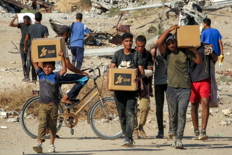 Des Palestiniens portent des cartons d'aide humanitaire reçus dans un centre de distribution géré par la Fondation humanitaire de Gaza (GHF), alors qu'ils traversent le