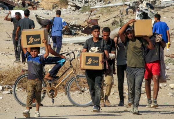 Des Palestiniens portent des cartons d'aide humanitaire reçus dans un centre de distribution géré par la Fondation humanitaire de Gaza (GHF), alors qu'ils traversent le "corridor de Netzarim", dans le centre de la bande de Gaza, le 22 août 2025