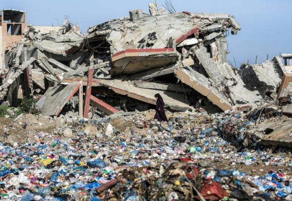 Une Palestinienne marche entre des détritus et un immeuble détruit, dans le camp de réfugiés de Nousseirat, dans le centre de la bande de Gaza, le 29 janvier 2026
