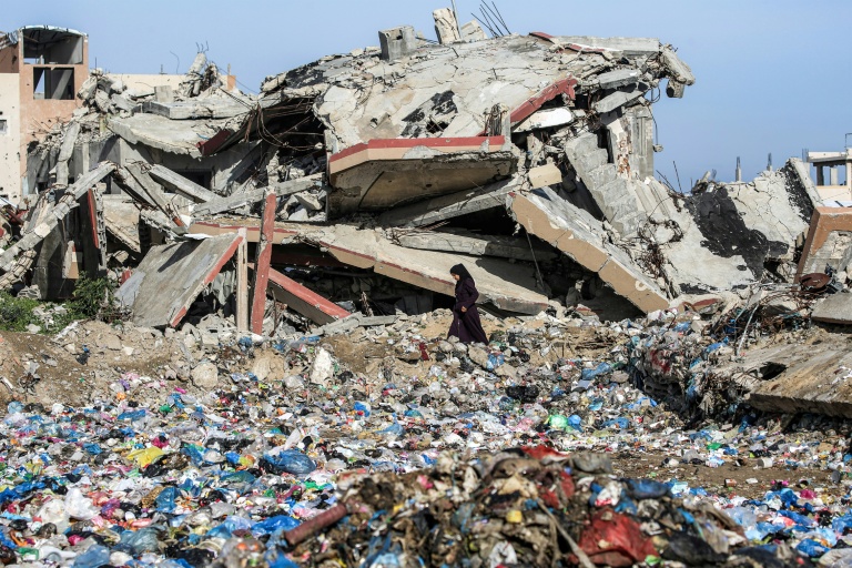 Une Palestinienne marche entre des détritus et un immeuble détruit, dans le camp de réfugiés de Nousseirat, dans le centre de la bande de Gaza, le 29 janvier 2026
