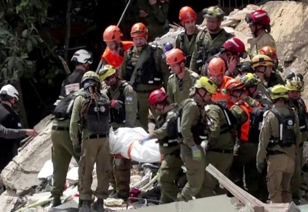 Image tirée d'une vidéo d'AFPTV montrant des équipes de secours  sortant les corps de victimes des décombres d'un immeuble résidentiel détruit par une attaque de missile iranienne dans la ville de Haïfa, dans le nord d'Israël, le 6 avril 2026
