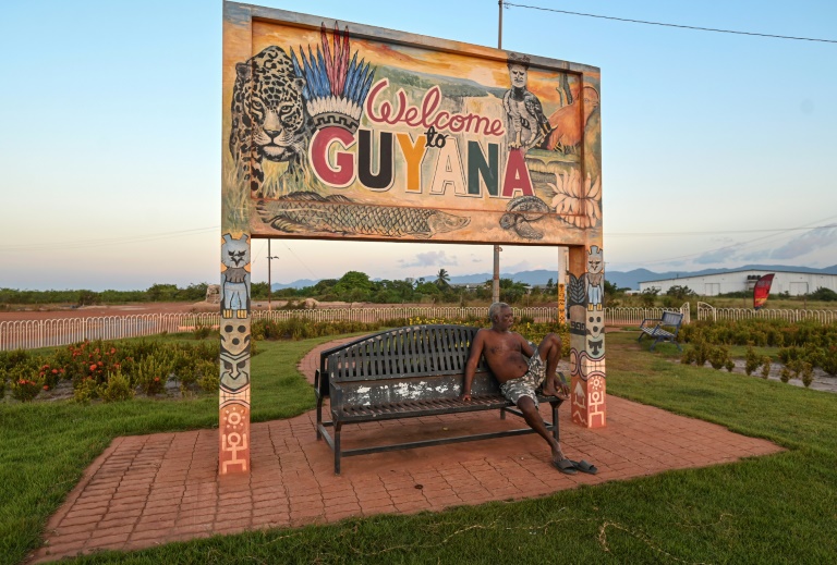 Un homme assis sur un banc sous un panneau à la frontière entre le Guyana et le Brésil, le 27 août 2025 près de Lethem, dans le sud-ouest du Guyana