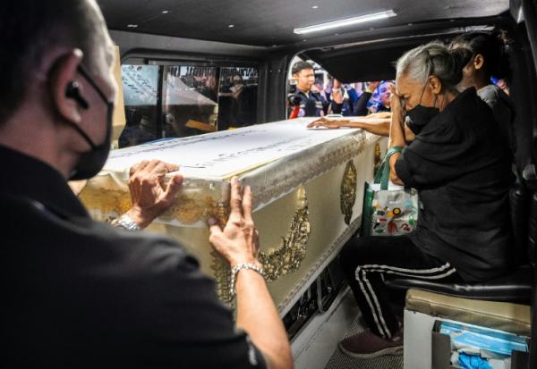 Une proche endeuillée accompagne le cercueil contenant la dépouille d'une victime de l'incendie d'un bar, dans un fourgon funéraire, le 14 juillet 2026 à l'hôpital général de la police de Bangkok, en Thaïlande