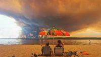 Des personnes sur la plage du Moutchic à Lacanau, dans le sud-ouest de la France, le 24 juillet 2026, tandis que des nuages de fumée d'un incendie s’élèvent dans le ciel 