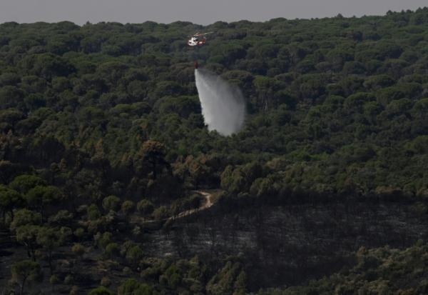 Un hélicoptère de lutte contre les incendies largue de l'eau pour rafraîchir une zone touchée par des feux de forêt à l'ouest de Madrid, le 28 juillet 2026