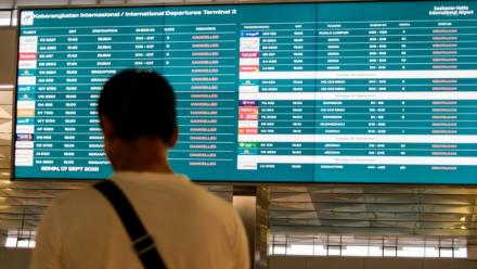 Un passager bloqué à l'aéroport international Soekarno-Hatta en raison de l'éruption du volcan Anak Krakatau, regarde un écran d'information sur les vols, le 7 septembre 2026 à Tangerang, en Indonésie