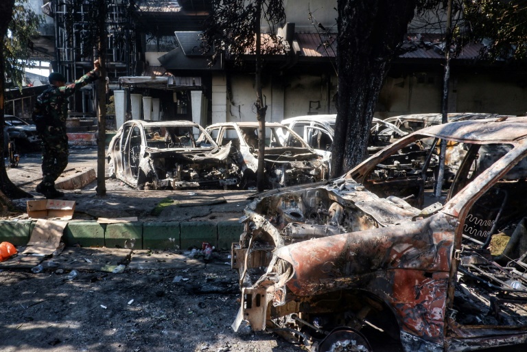 Des carcasses de voitures incendiées près du conseil provincial et local de Makassar, principale ville indonésienne des Célèbes du sud théâtre de manifestations qui ont dégénéré après la mort d'un taxi-moto écrasé par un véhicule de police, le 30 août 2025
Cars and the Makassar City Council building, which were set on fire the previous night during a protest, are seen in Makassar, South Sulawesi, on August 30, 2025. At least three people were killed by a fire started by protesters at the council building in eastern Indonesia's Makassar city, a local official told AFP on August 30, after demonstrations across the country following the death of a motorcycle taxi driver hit by a police vehicle.