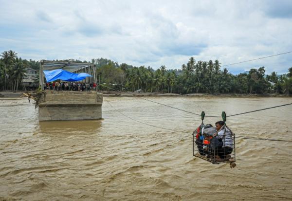 Des villageois utilisent une cabine sur câble pour traverser une rivière après la destruction d'un pont à Bireuen, en Indonésie, le 2 décembre 2025