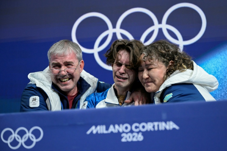 Le Kazakhstanais Mikhail Shaidorov (au centre) avec ses entraîneurs au moment où sa note s'affiche après son programme libre de patinage artistique le 13 février 2026 où il a décroché l'or à la surprise générale
