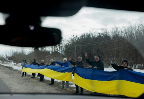 Des personnes tiennent un drapeau ukrainien le long d'une route pour accueillir un convoi de soldats libérés par les Russes après un échange de prisonniers, le 6 mars 2026 dans un lieu non précisé dans le nord de l'Ukraine