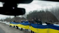 Des personnes tiennent un drapeau ukrainien le long d'une route pour accueillir un convoi de soldats libérés par les Russes après un échange de prisonniers, le 6 mars 2026 dans un lieu non précisé dans le nord de l'Ukraine
