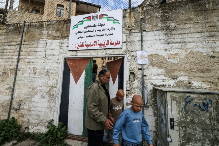Les jumeaux Ahmad (d) et Mohammad, accompagnés par leur père Ibrahim al-Hajj, sortent de leur école à Naplouse, le 10 février 2026 en Cisjordanie occupée