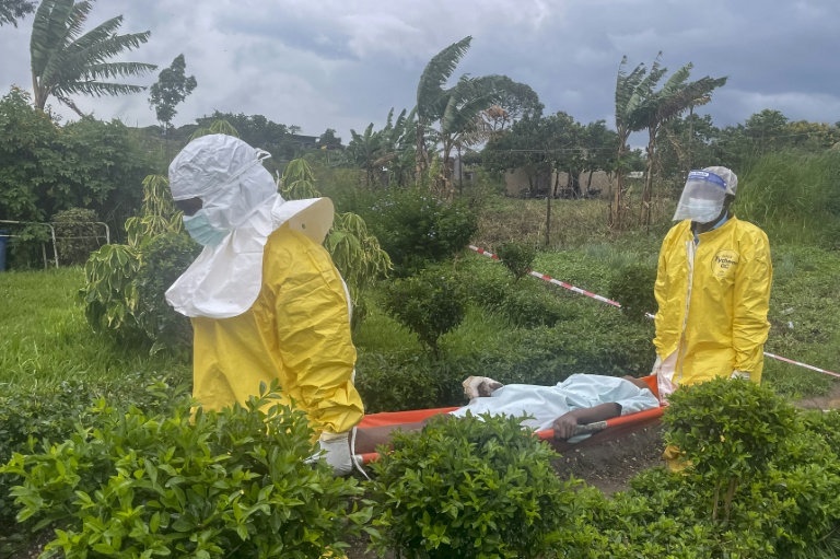Des membres du personnel soignant en combinaison de protection transportent un patient à Rwampara après qu'un hôpital a été incendié par des manifestants qui s'étaient vu refuser l'accès aux corps de leurs proches décédés du virus Ebola, le 21 mai 2026 en RDC