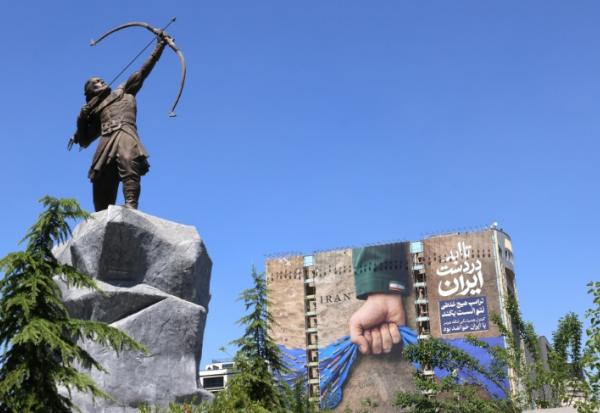 Une sculpture d'Arash l'Archer, figure légendaire de la mythologie persane, et une affiche géante représentant le détroit d'Ormuz avec l'inscription "À jamais dans la main de l'Iran", place Vanak à Téhéran, le 25 mai 2026