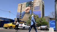 Des passants près d'un panneau d'affichage sur la façade d'un immeuble représentant le détroit d'Ormuz avec une inscription en persan disant "À jamais dans la main de l'Iran", place Vanak à Téhéran, le 25 mai 2026