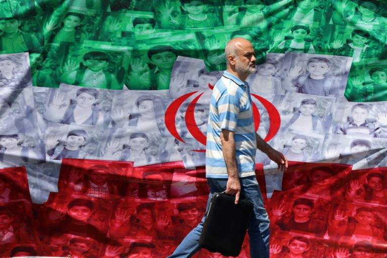 Un homme passe devant un drapeau iranien installé le long de la route à Téhéran le 29 avril 2026